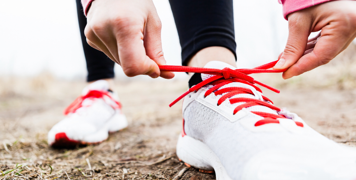Person tying red shoelace on white sneakers.